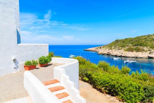 White house and view of fishing boats on sea in Cala Portinatx Bay in Ibiza island White house and view of fishing boats on sea in Cala Portinatx Bay in Ibiza island